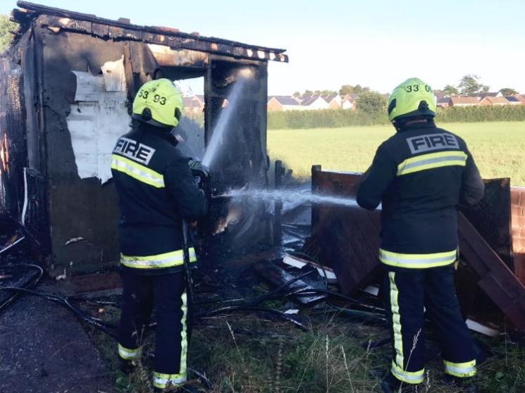 Two firefighters extinguishing a shed that had been burned black from an out of control bonfire.